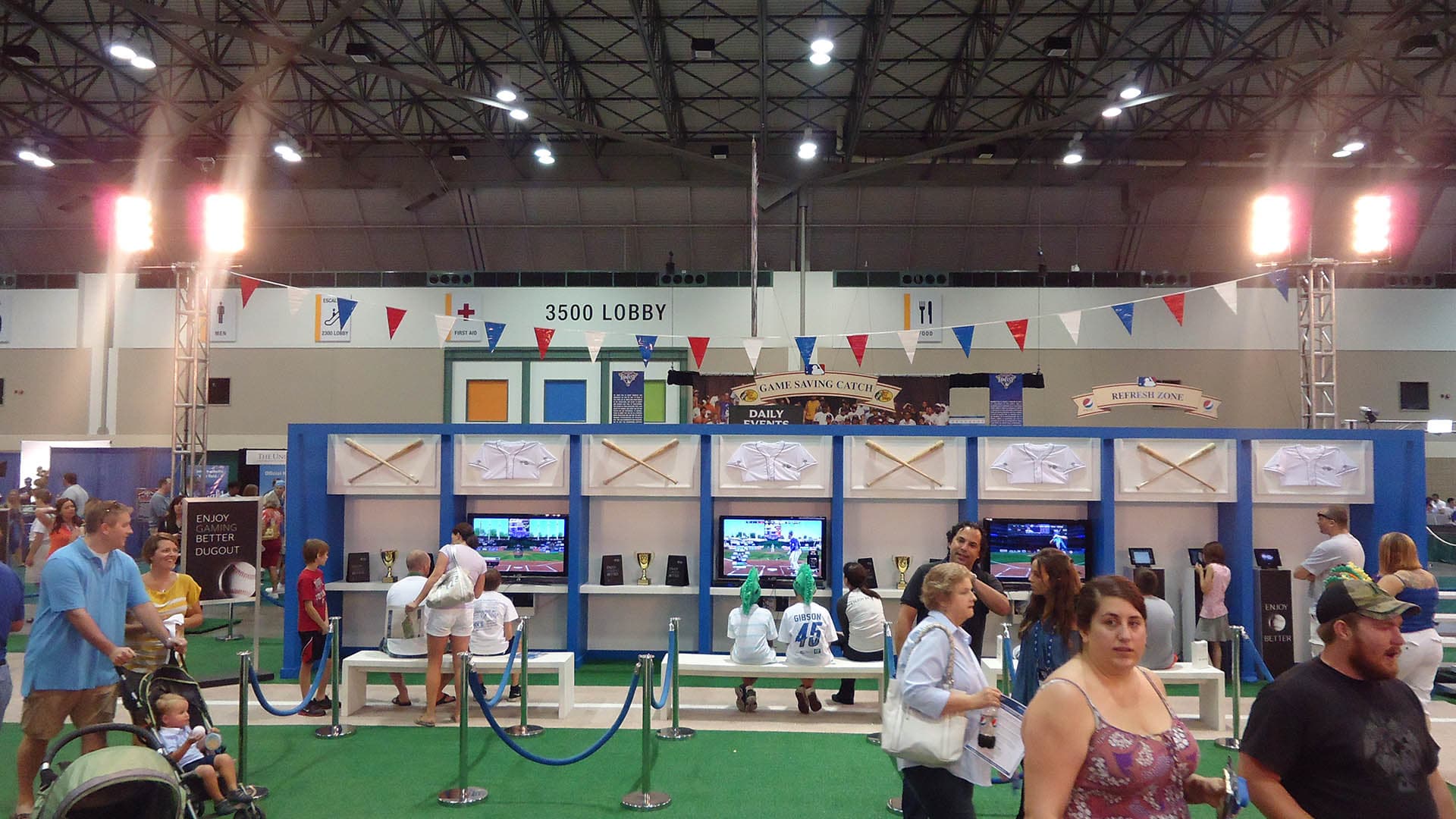 A wide shot of the front of the MLB Network booth with people walking by.