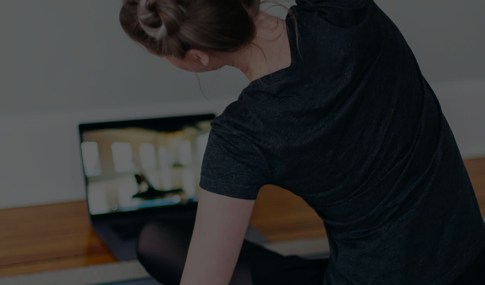 A person doing fitness exercises on the floor while watching an online class on a laptop